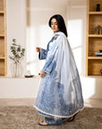 Woman in a traditional outfit standing in a room with wooden shelves and decor.