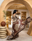 Woman in a patterned dress standing in a room with wooden arches and shelves.