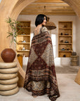 Woman in a patterned dress standing in a room with wooden shelves and decor.
