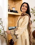 Woman in traditional attire standing next to a wooden shelf with books and decorative items.