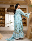 Woman in a light blue floral dress standing in a room with wooden shelves.