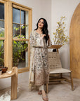 Woman in a brown floral dress standing in a room with wooden furniture and plants.
