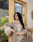 Woman in a brown patterned dress standing indoors with plants and a window in the background