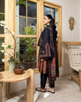 Woman in a patterned outfit standing in a room with wooden furniture and plants.