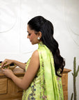 Woman in a green saree with floral patterns standing next to a wooden cabinet.