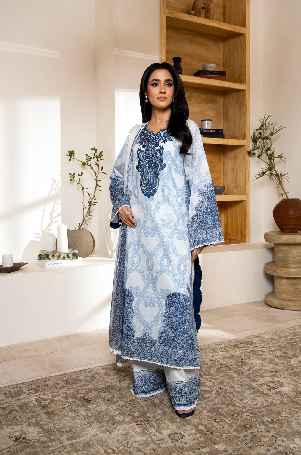 Woman wearing a blue and white embroidered traditional outfit in a home setting.