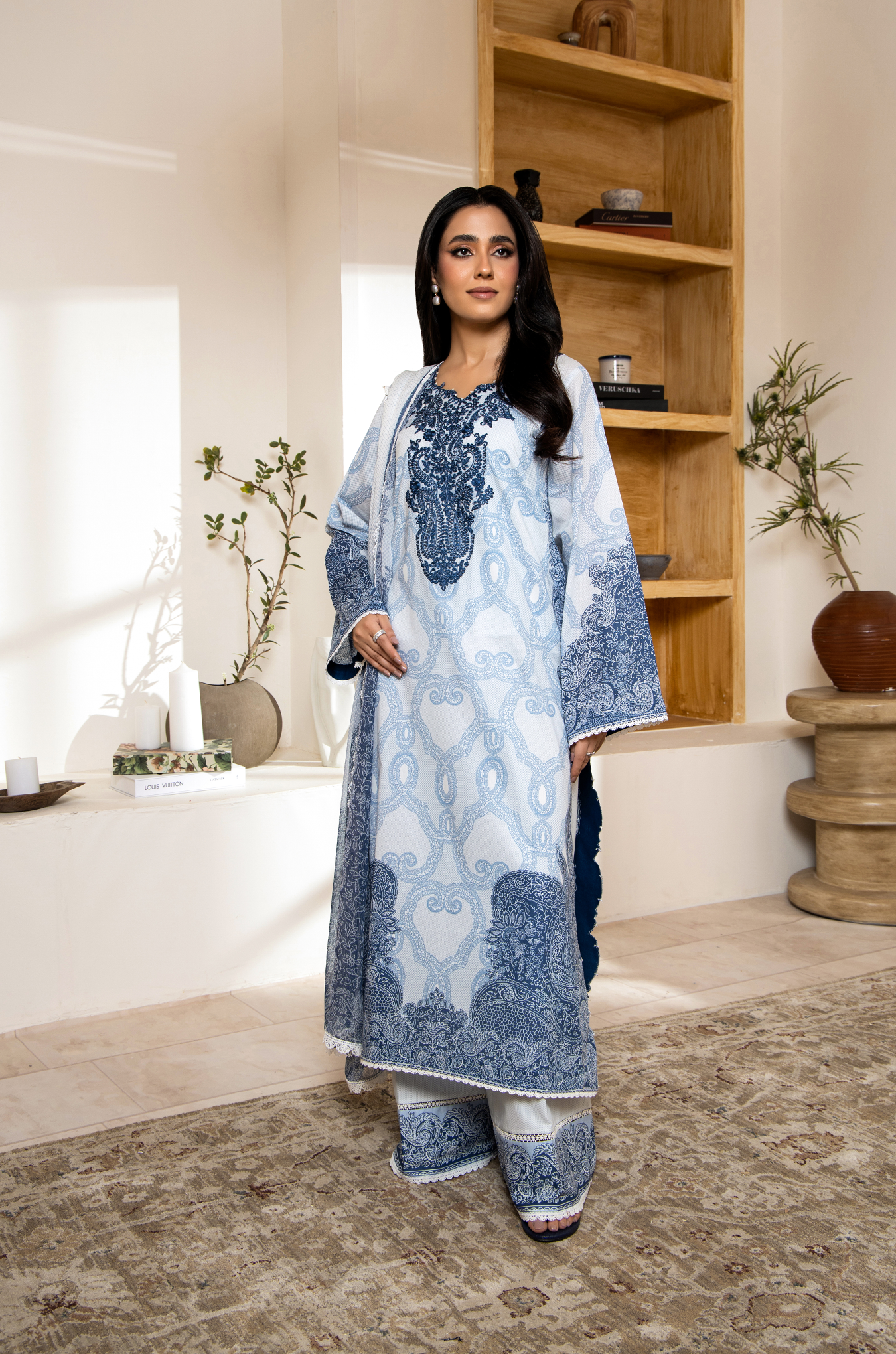 Woman wearing a blue and white embroidered traditional outfit in a home setting.