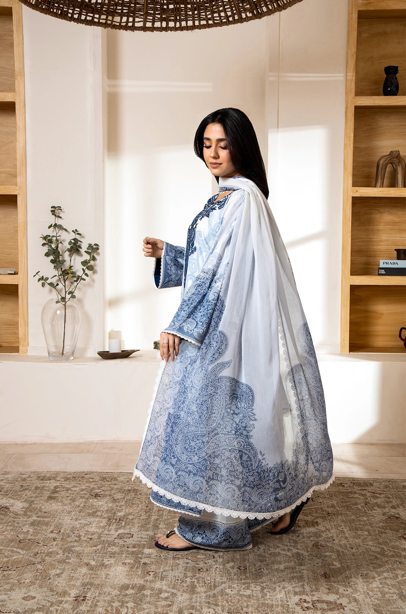 Woman in a traditional outfit standing in a room with wooden shelves and decor.