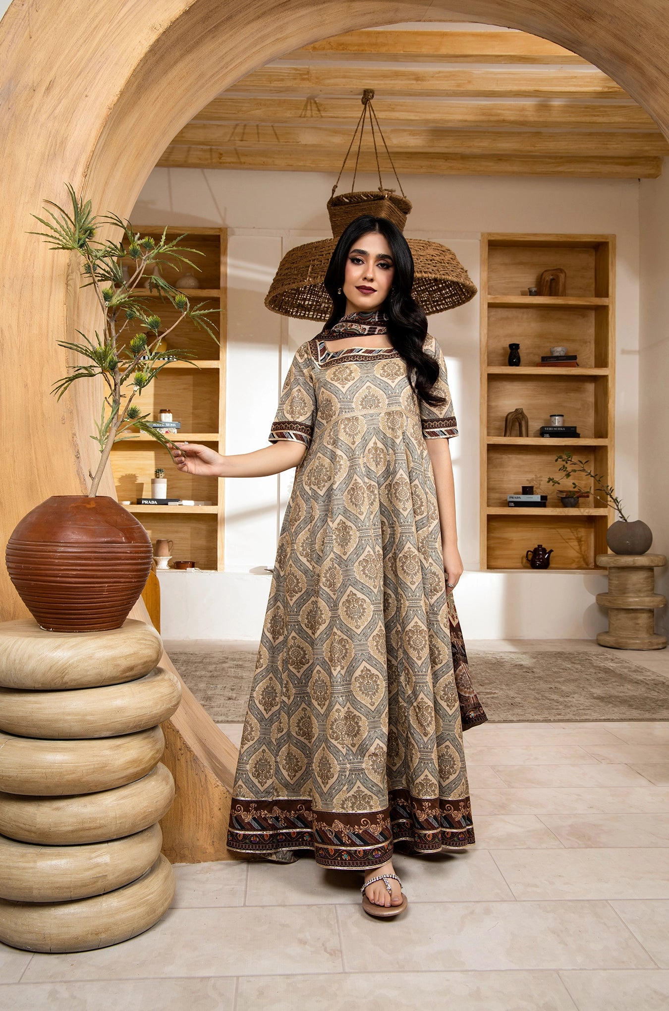 Woman in a patterned dress standing in a room with wooden shelves and decorative items.