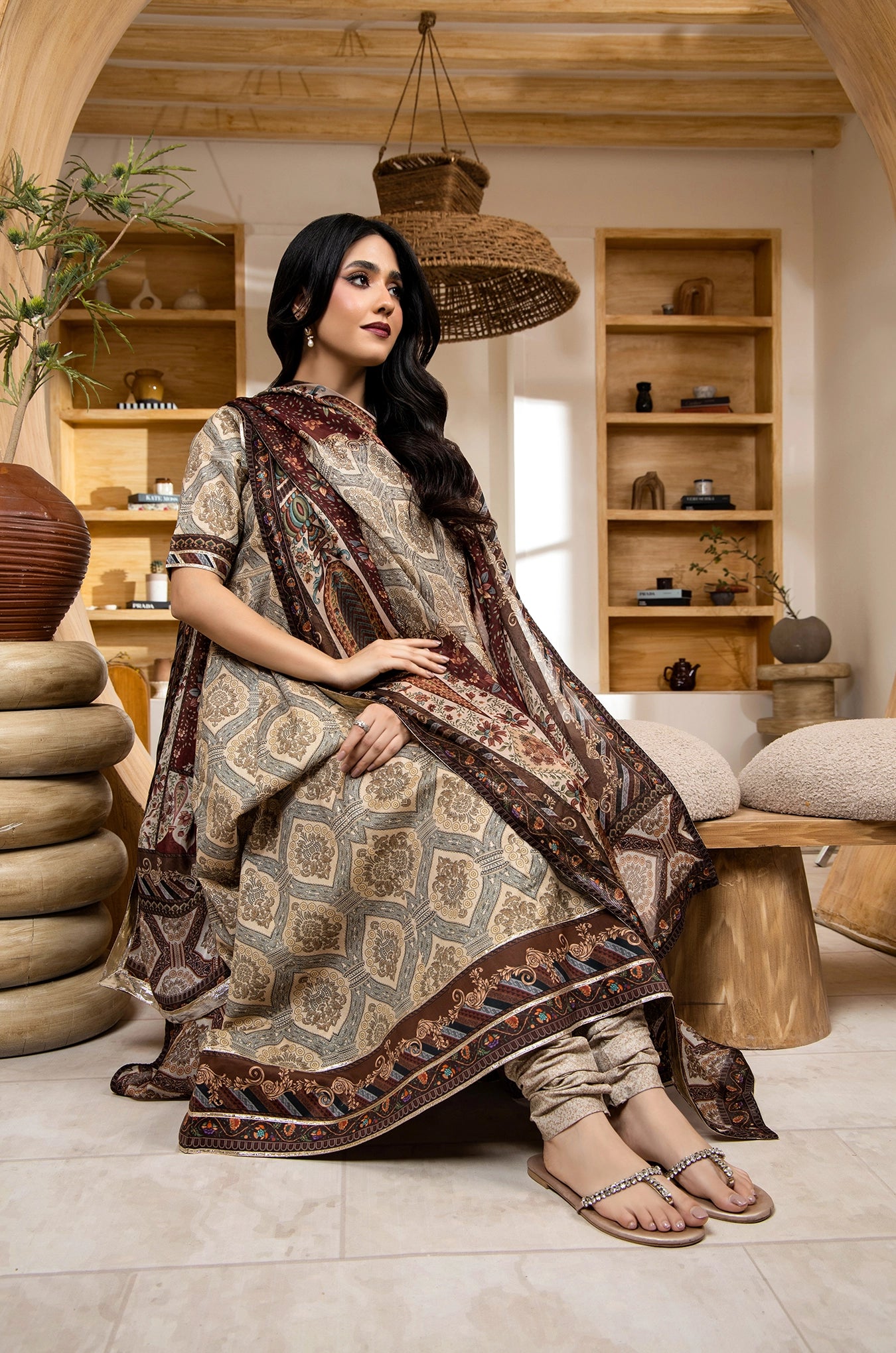 Woman in a patterned dress sitting in a cozy room with wooden shelves and decor.