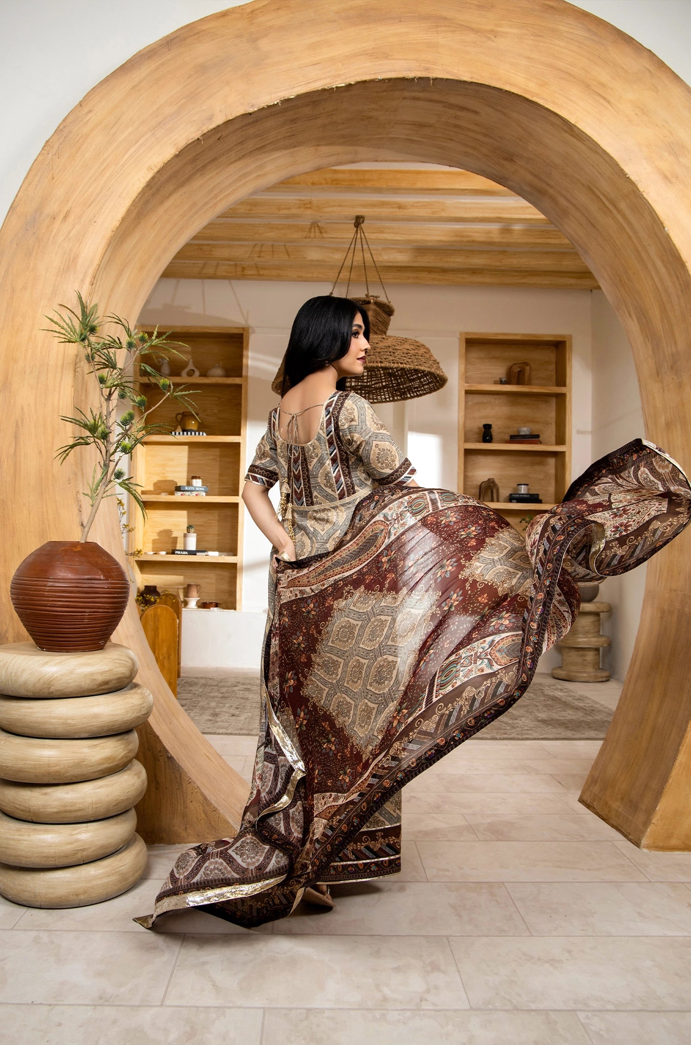 Woman in a patterned dress standing in a room with wooden arches and shelves.