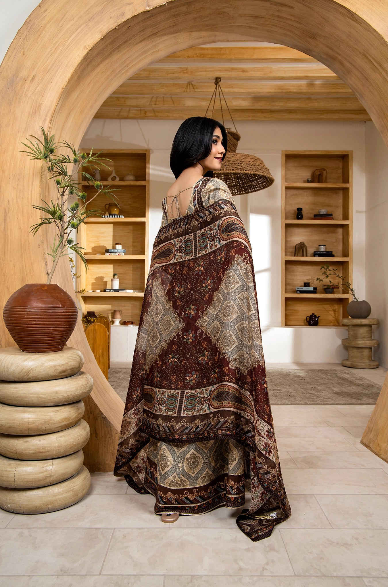 Woman in a patterned dress standing in a room with wooden shelves and decor.