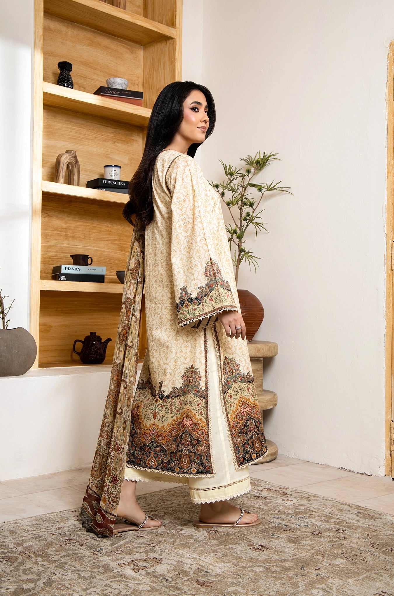 Woman in a traditional outfit standing in a room with wooden shelves and decor.