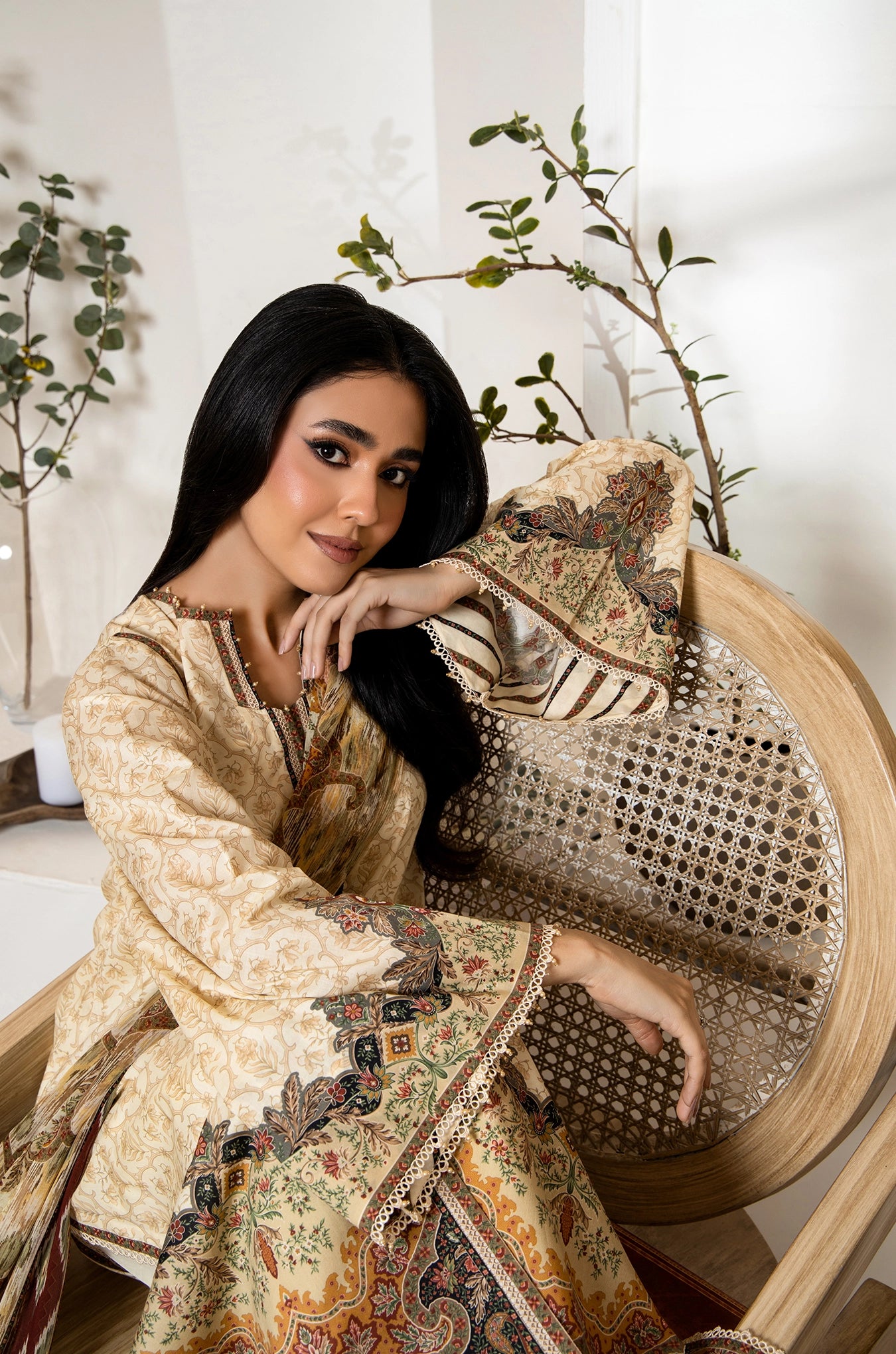 Woman in traditional attire sitting on a decorative chair with plants in the background
