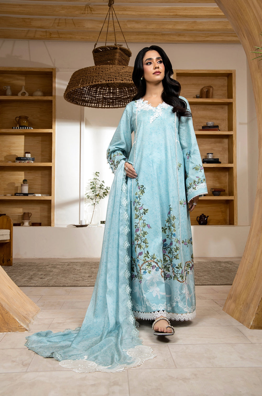 Woman in a light blue embroidered traditional outfit standing in a room with wooden shelves.