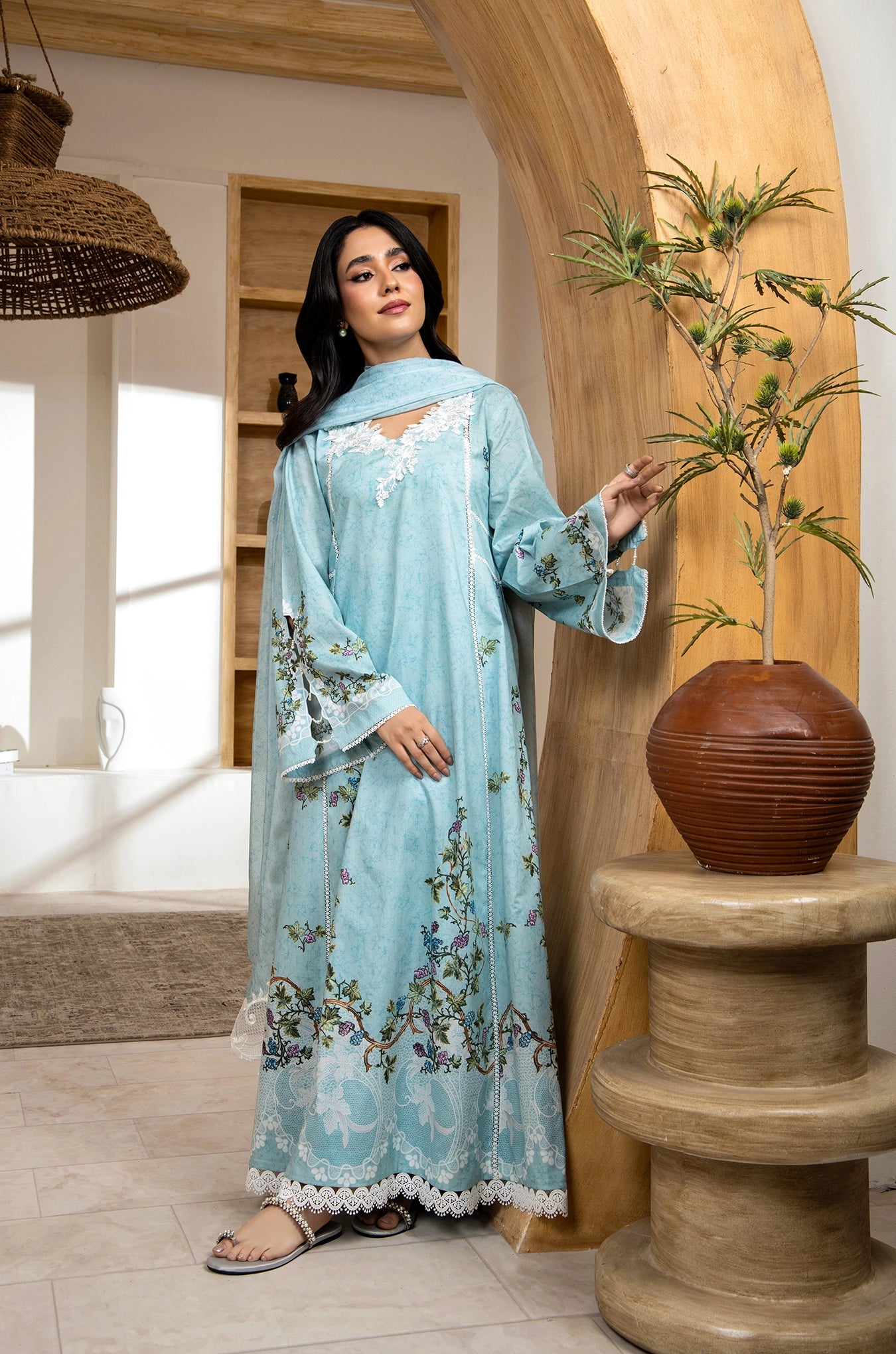 Woman in a light blue floral dress standing in a room with wooden arch and vase.