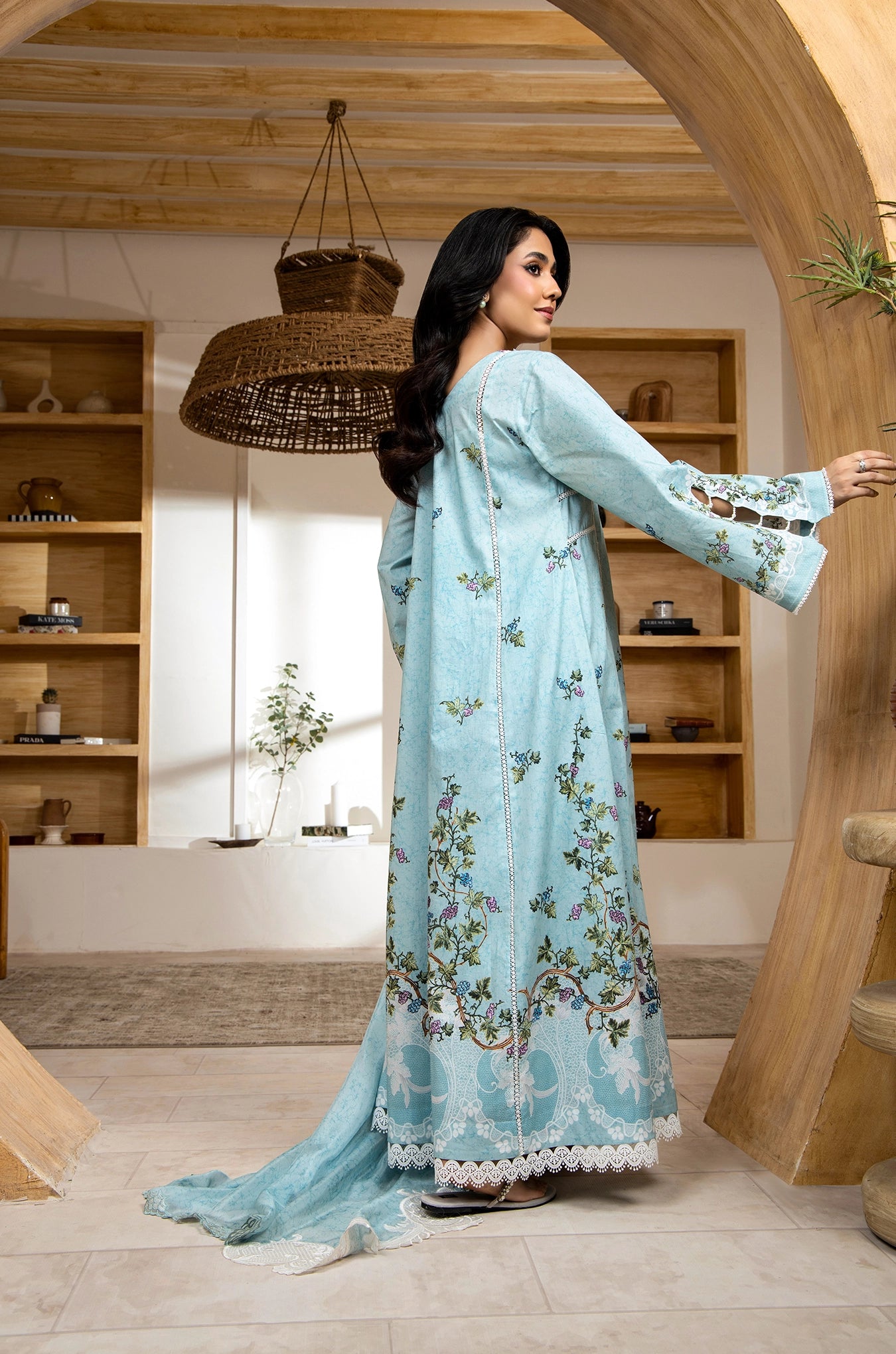 Woman in a light blue floral dress standing in a room with wooden shelves.