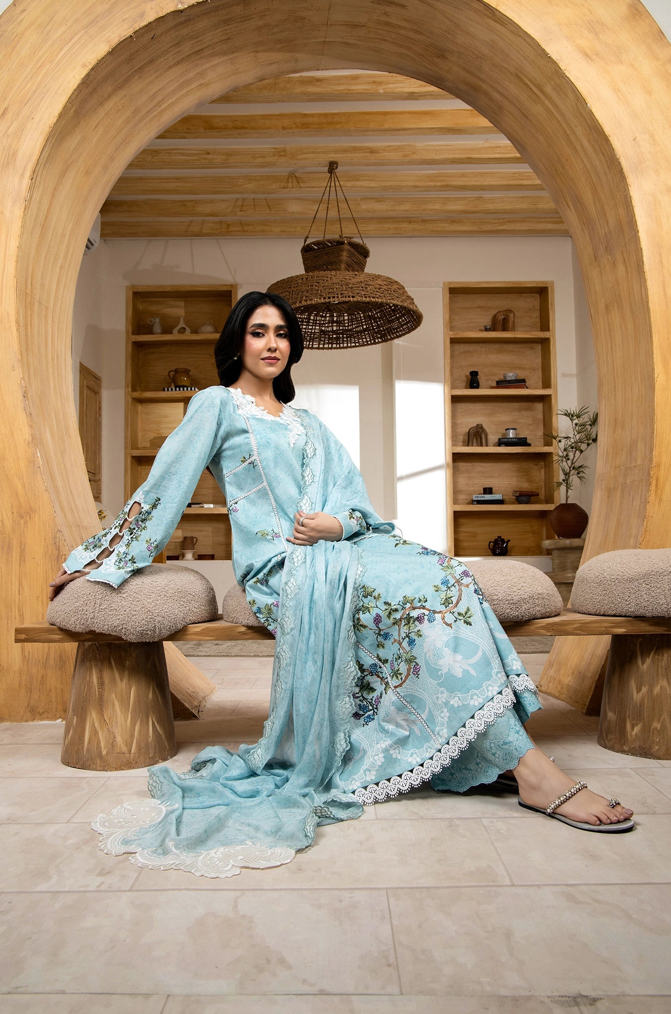 Woman in a light blue embroidered dress sitting in a modern interior setting.