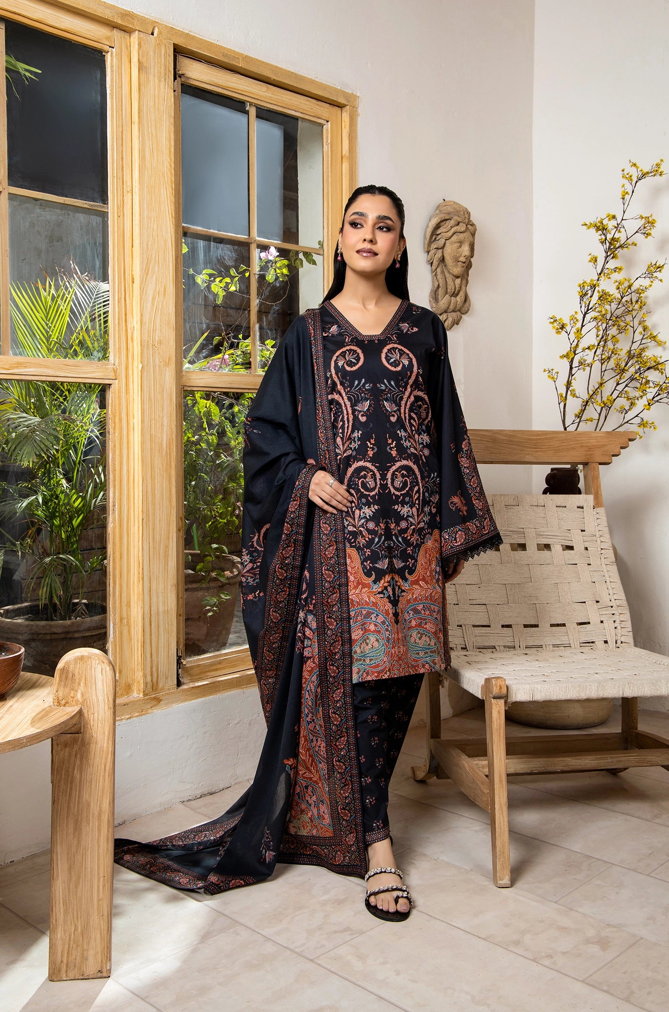 Woman in a dark floral outfit standing in a room with wooden furniture and plants.