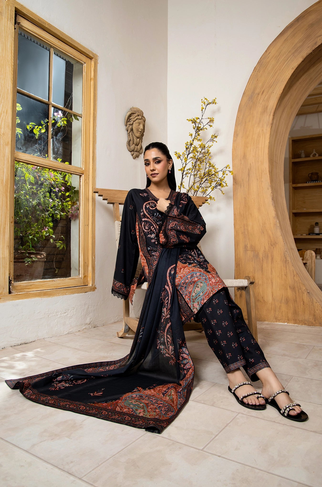 Woman in a dark patterned outfit standing in a room with a window and wooden arch.