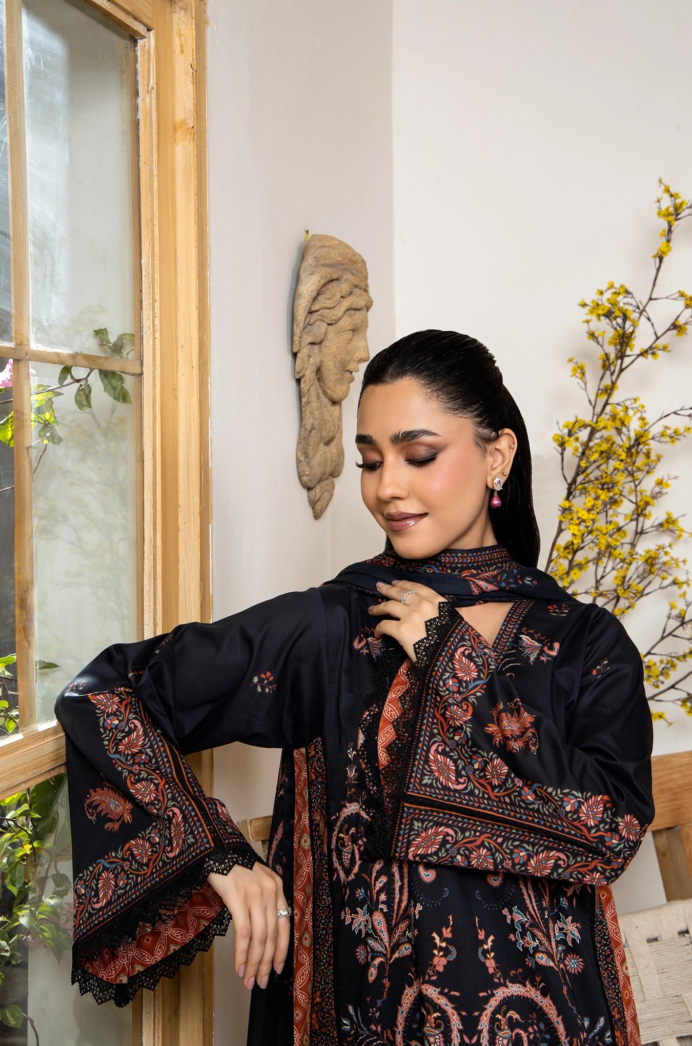 Woman wearing a black and red patterned dress standing indoors with decorative elements.
