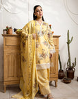 Woman in a yellow floral outfit standing in a room with wooden furniture and plants.