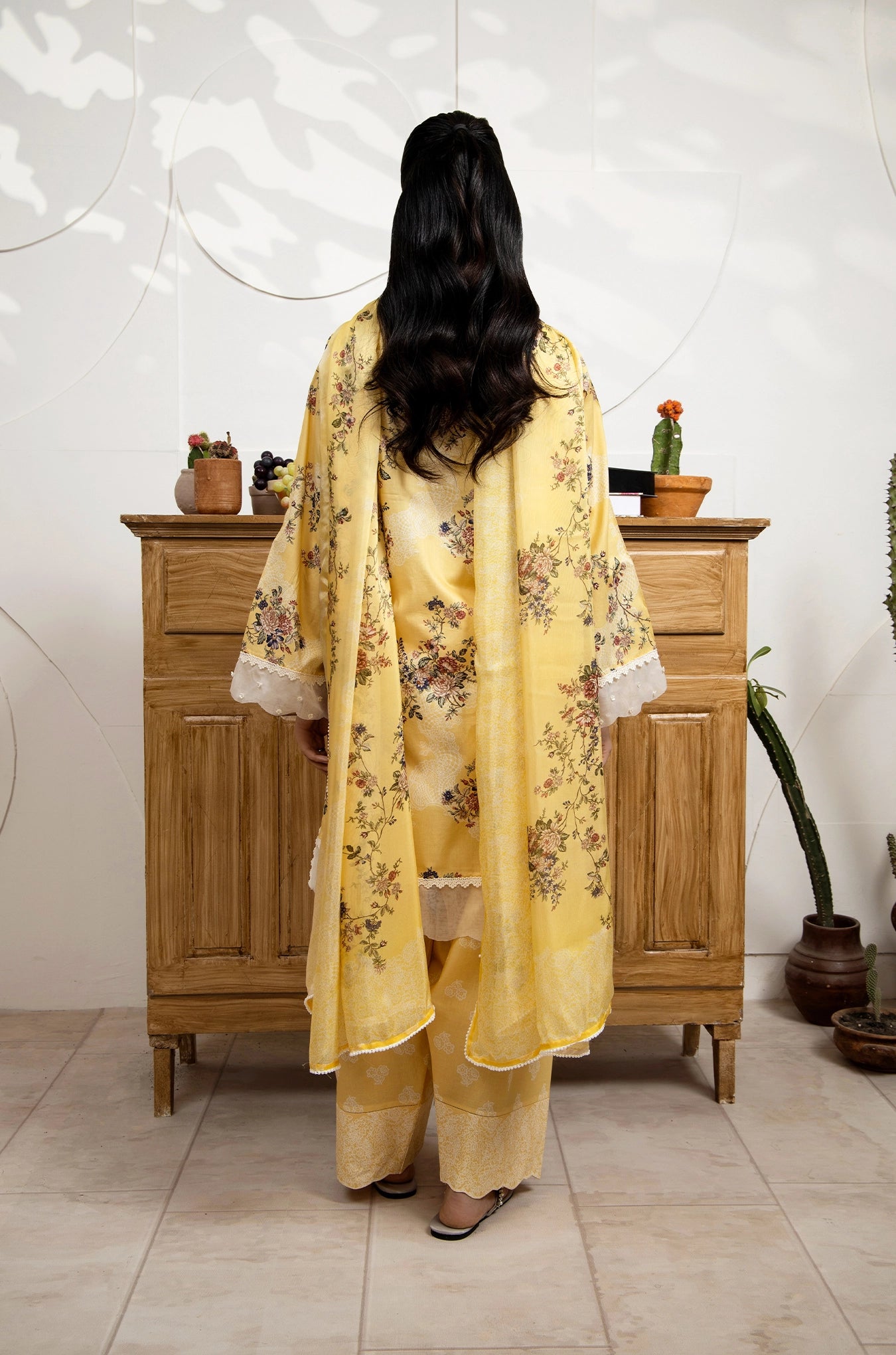 Person wearing a yellow floral outfit standing in front of a wooden cabinet.