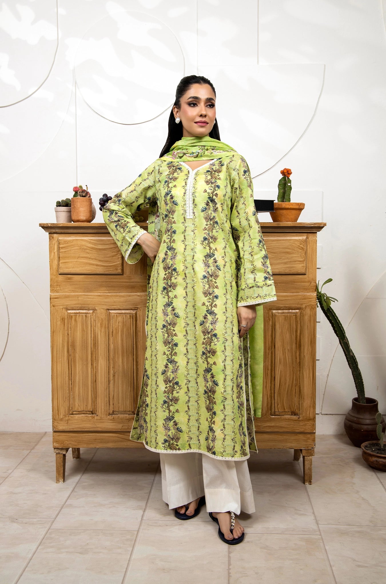 Woman in a green floral dress standing in front of a wooden cabinet with decorative plants.