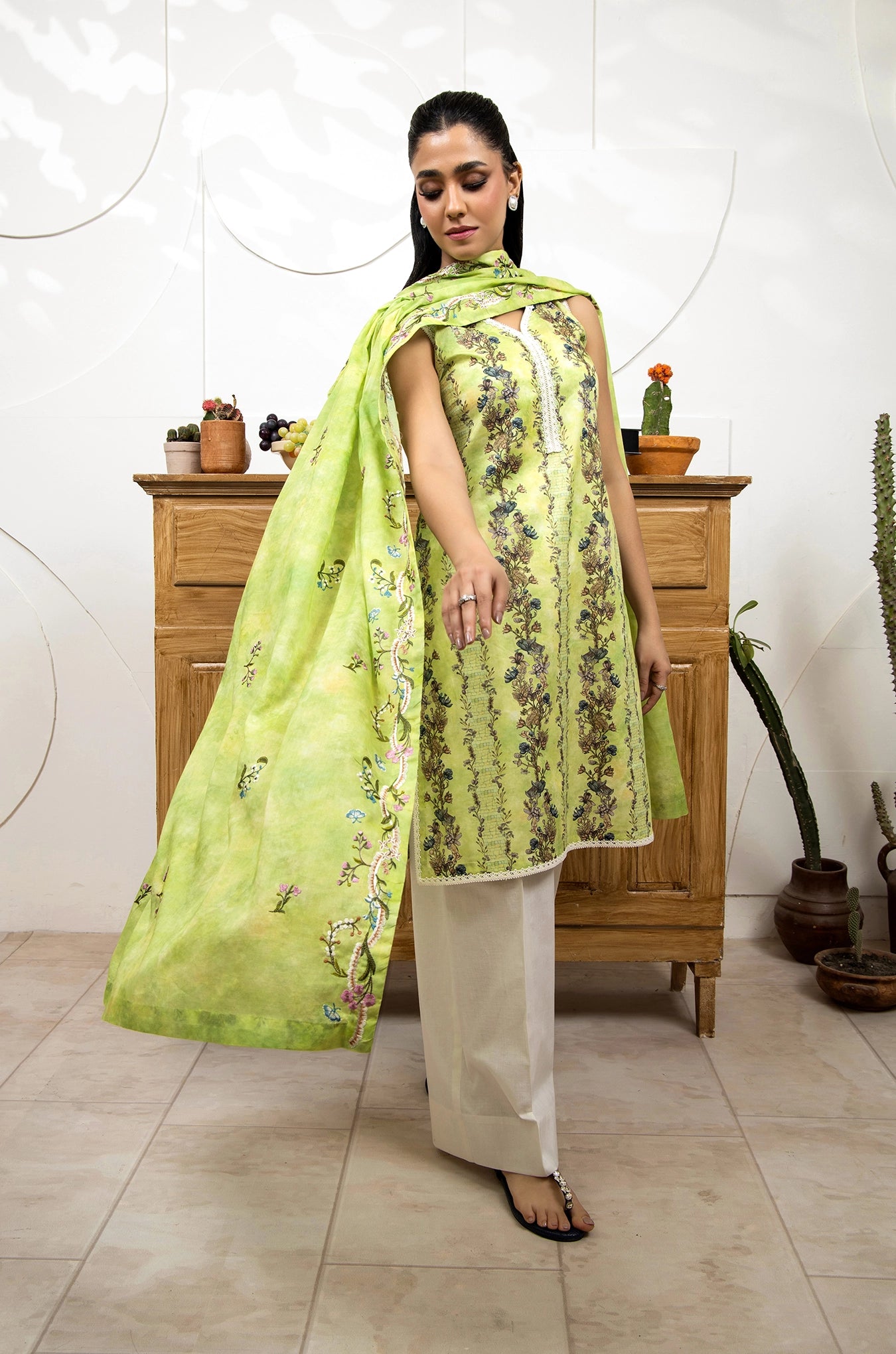 Woman wearing a green floral dress with a matching dupatta in a room setting.
