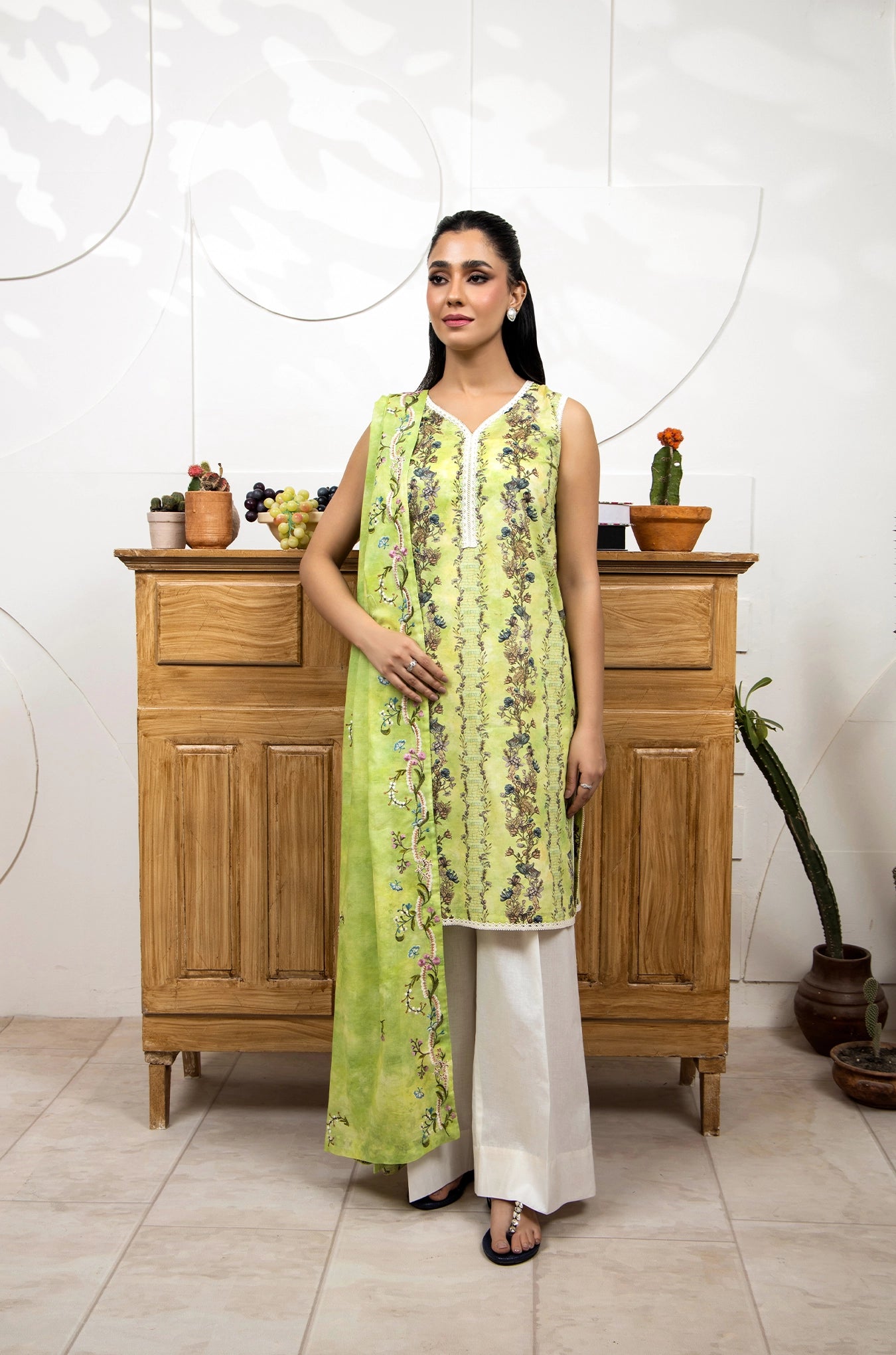 Woman in a green floral dress standing in front of a wooden cabinet with decorative items.