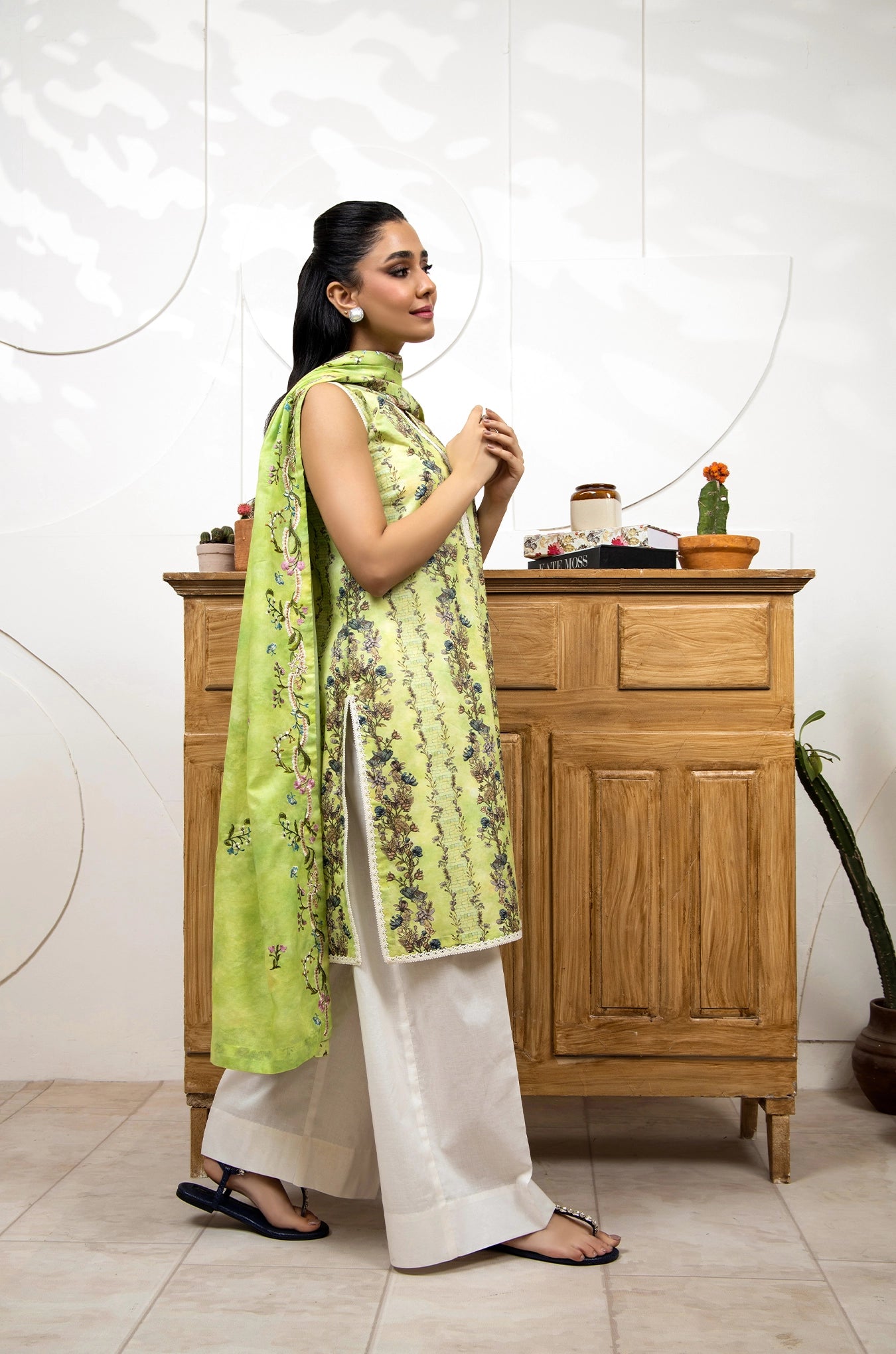 Woman in a green and white traditional outfit standing in front of a wooden cabinet.