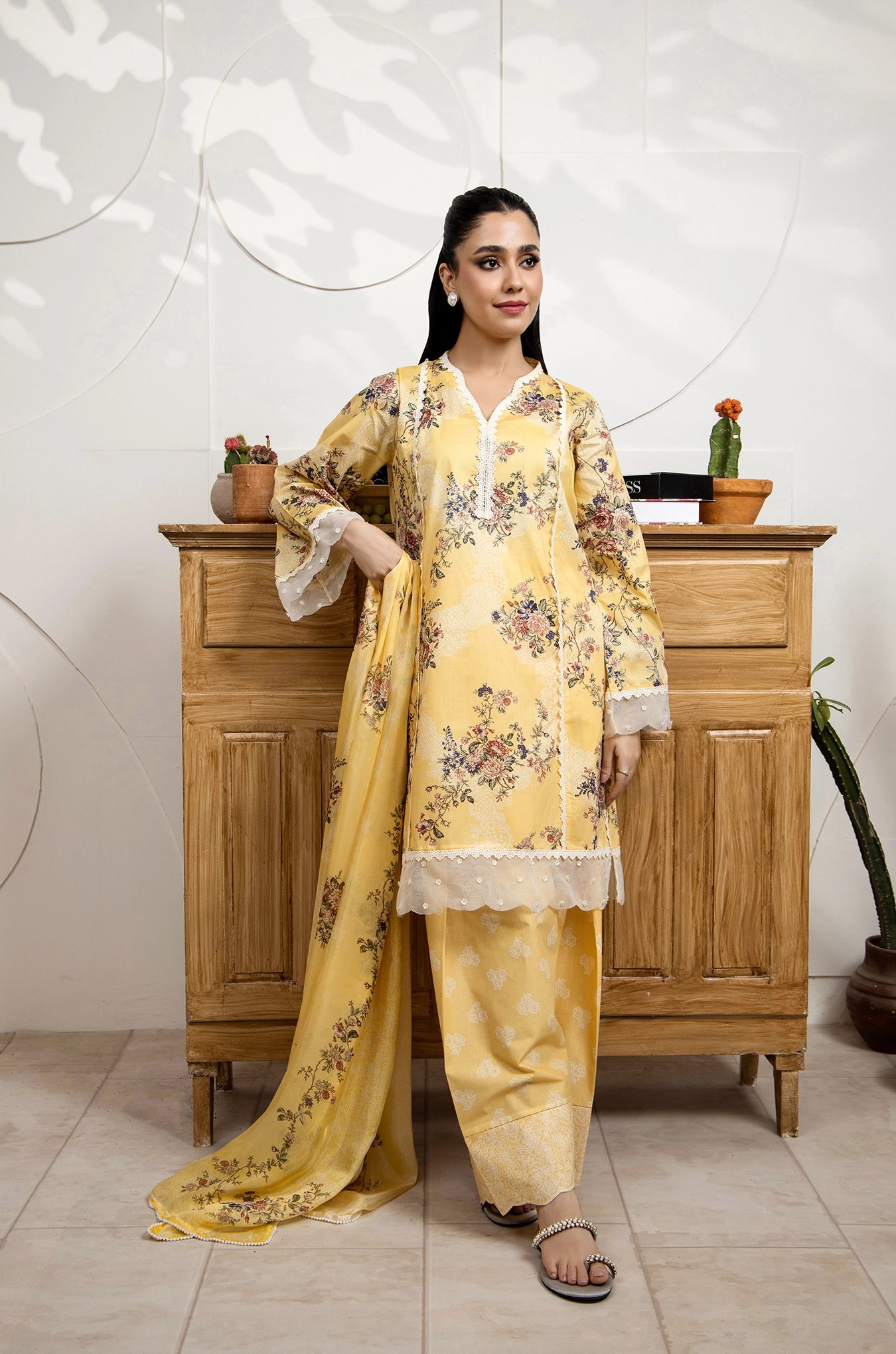 Woman in a yellow floral dress standing in front of a wooden cabinet.